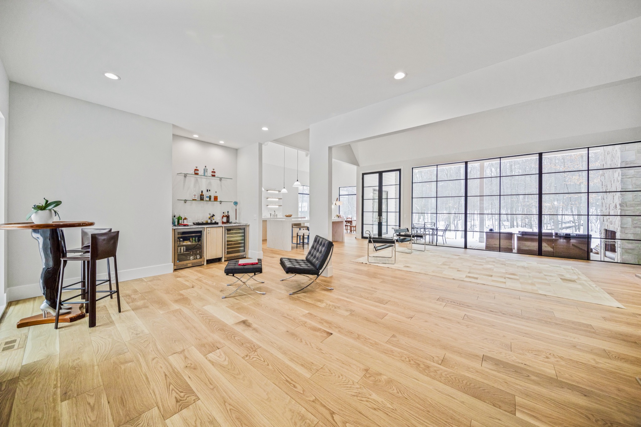 Lower level entertaining space with wet bar, wine cooler, glass shelving, and expansive glass curtain wall overlooking snowy woodland — luxury estate by Skoda Construction, Northeast Ohio
