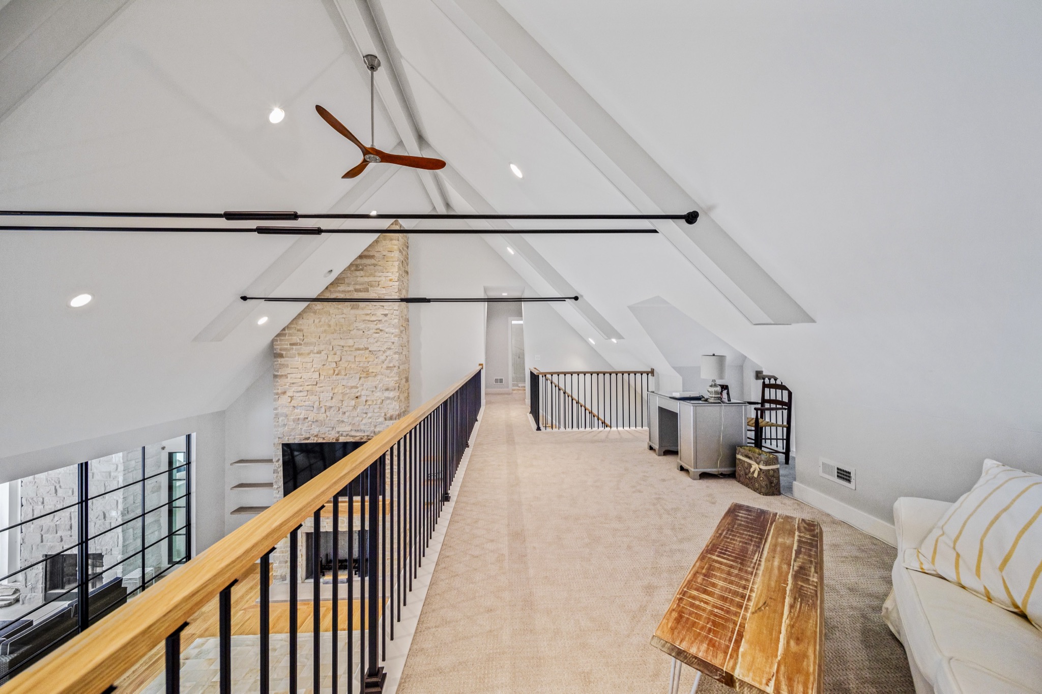 Loft walkway overlooking two-story great room with cathedral ceiling, exposed beams, stone fireplace chimney, and modern ceiling fan — luxury estate by Skoda Construction, Northeast Ohio