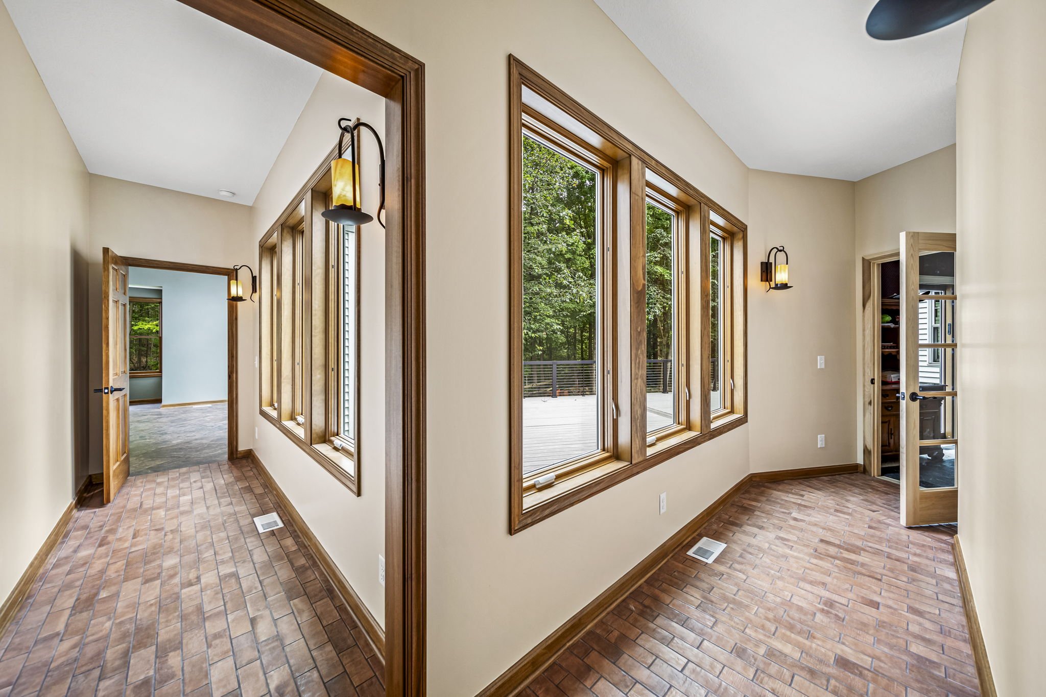 Craftsman hallway with herringbone brick floors, dark wood-framed windows with forest views, and wrought-iron wall sconces — custom home by Skoda Construction, Northeast Ohio