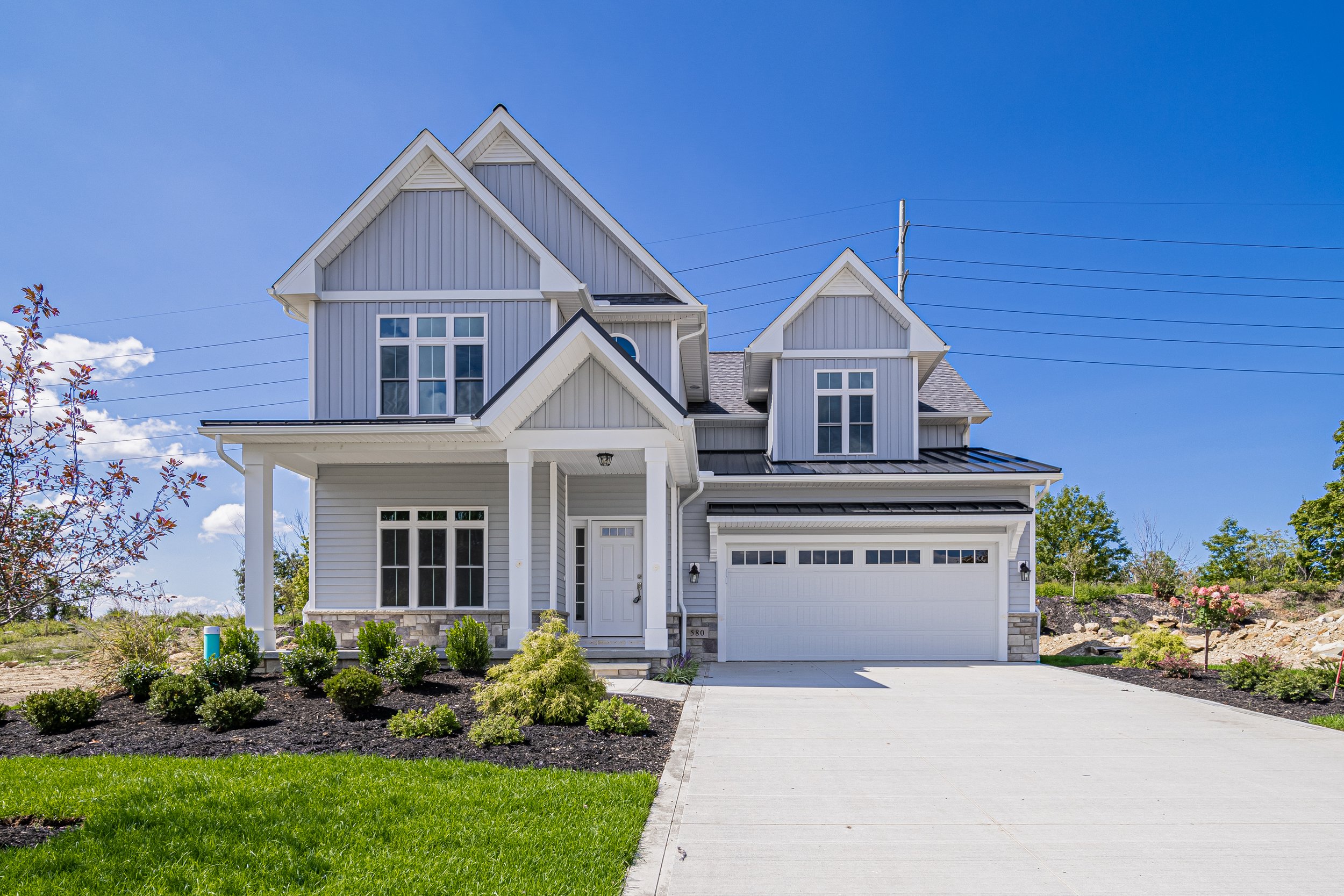 New construction custom home with gray board-and-batten siding, covered porch, and professional landscaping in Montebello community — Skoda Construction, Mayfield Village OH