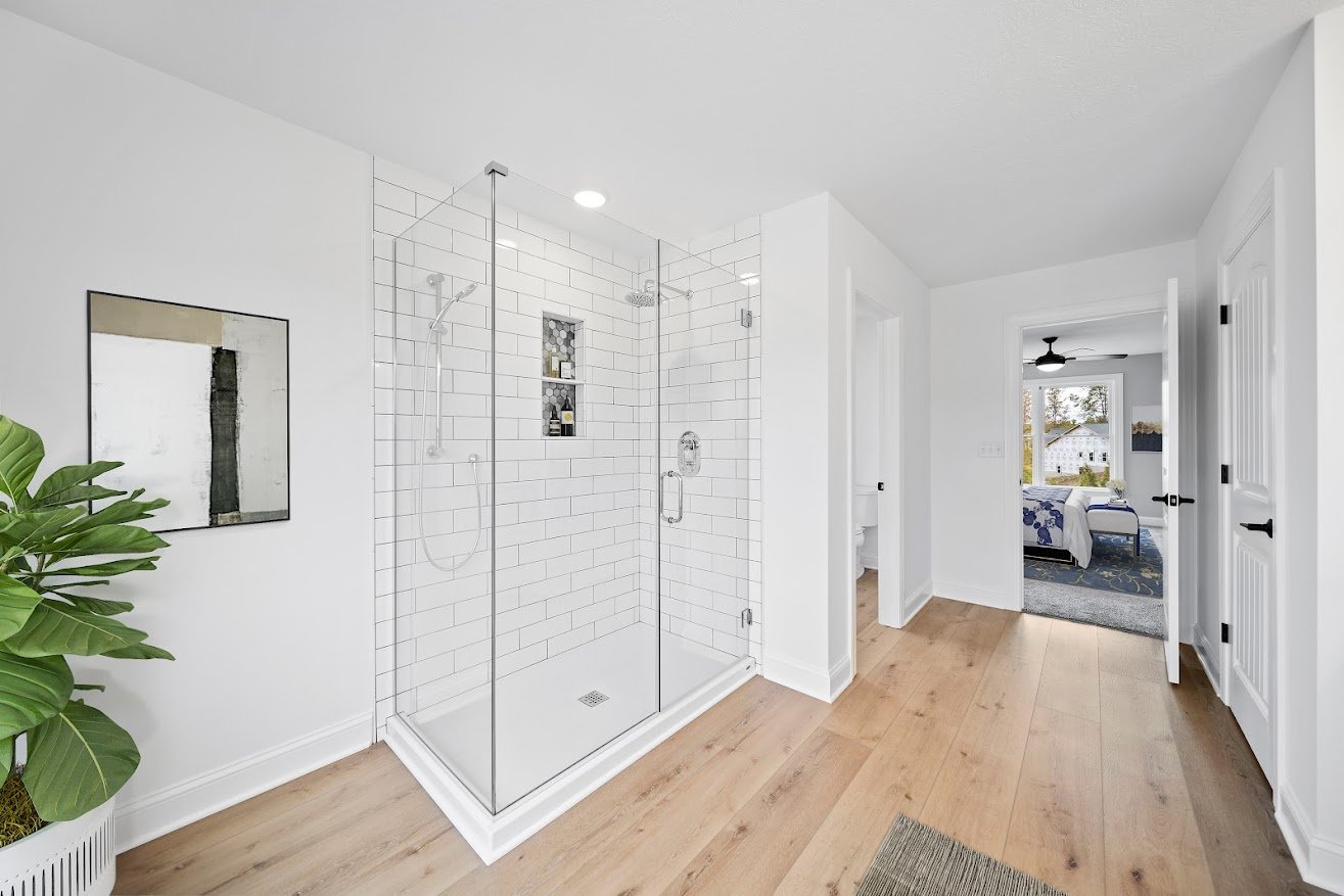 Modern bathroom with white subway tile walk-in shower, glass enclosure, and wide-plank hardwood floors — new construction by Skoda Construction, Northeast Ohio