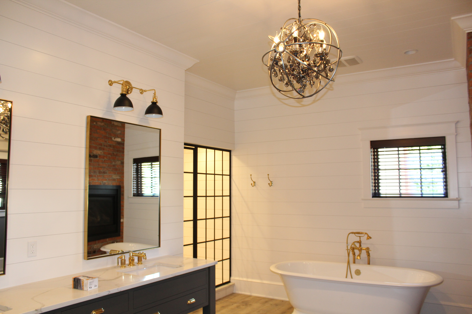 Luxury master bathroom with shiplap walls, freestanding clawfoot tub, orb chandelier, brass fixtures, and factory-window glass shower door — custom home by Skoda Construction, Northeast Ohio