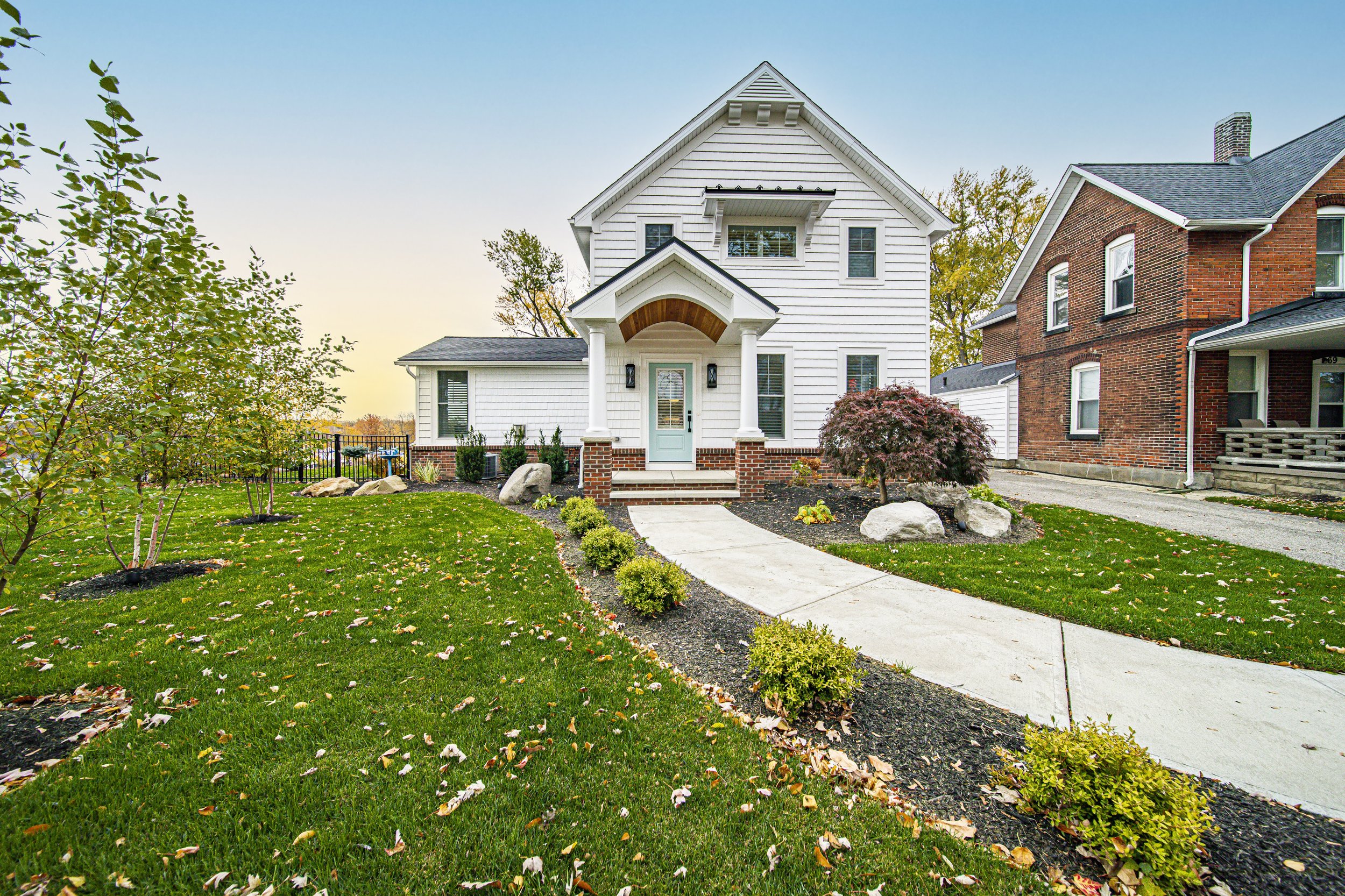Charming cottage home with arched doorway, landscaped front walk, and mature trees at golden hour — custom home by Skoda Construction, Northeast Ohio