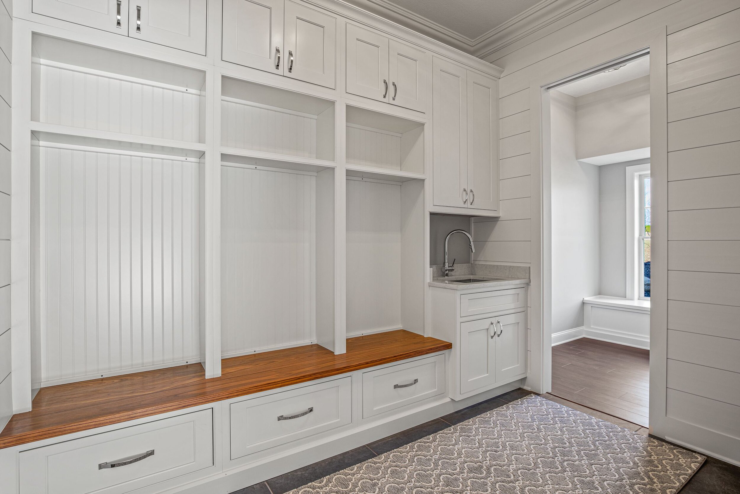 Custom mudroom with white built-in cubbies, walnut bench seat, upper storage cabinets, utility sink, and shiplap walls — luxury farmhouse by Skoda Construction, Northeast Ohio