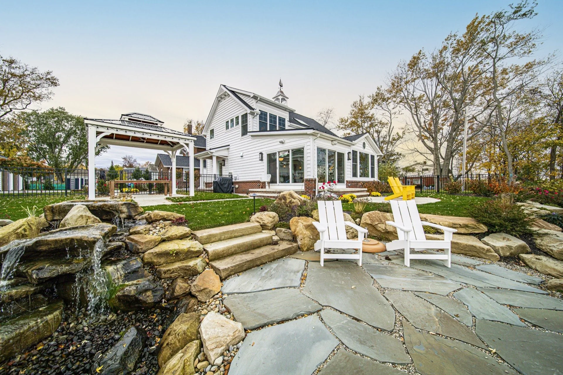 Outdoor living space with natural stone water feature, flagstone patio, Adirondack chairs, pergola, and pool — custom home backyard by Skoda Construction, Northeast Ohio